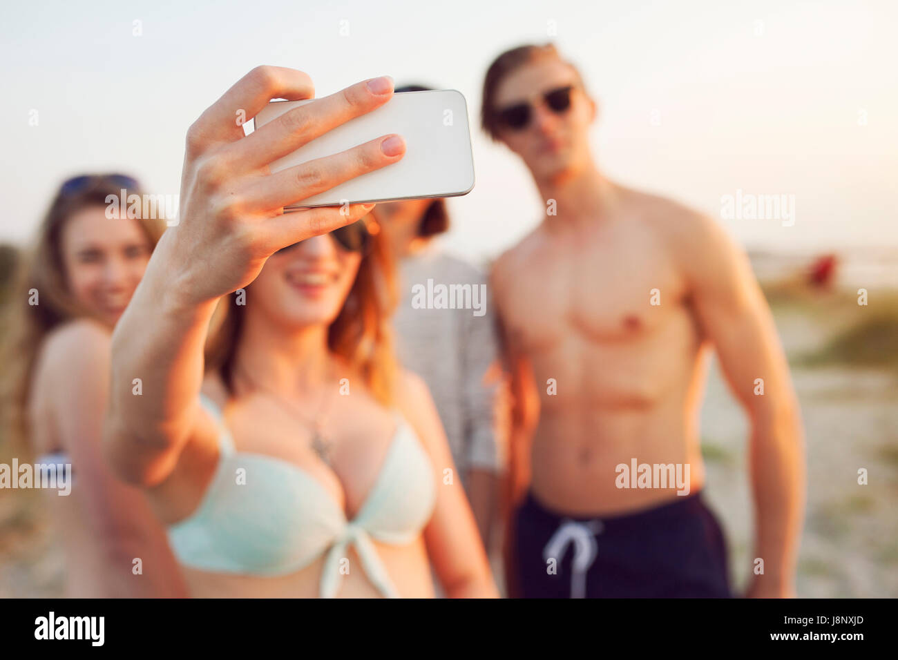 Les jeunes hommes, les jeunes femmes et teenage girl (16-17) prendre sur selfies beach Banque D'Images