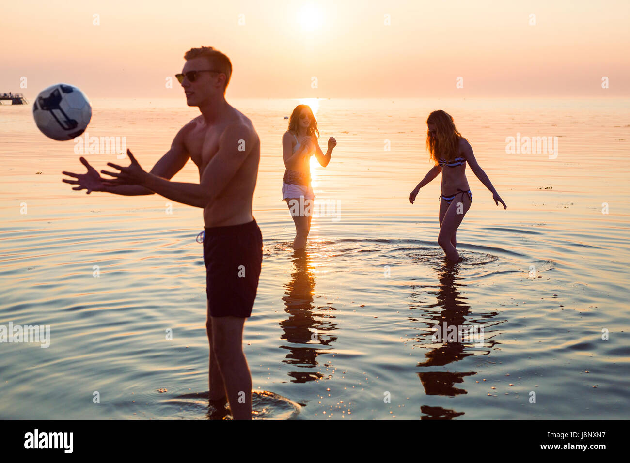 Jeune homme, jeune femme et teenage girl (16-17) jouer au volley-ball en mer au coucher du soleil Banque D'Images