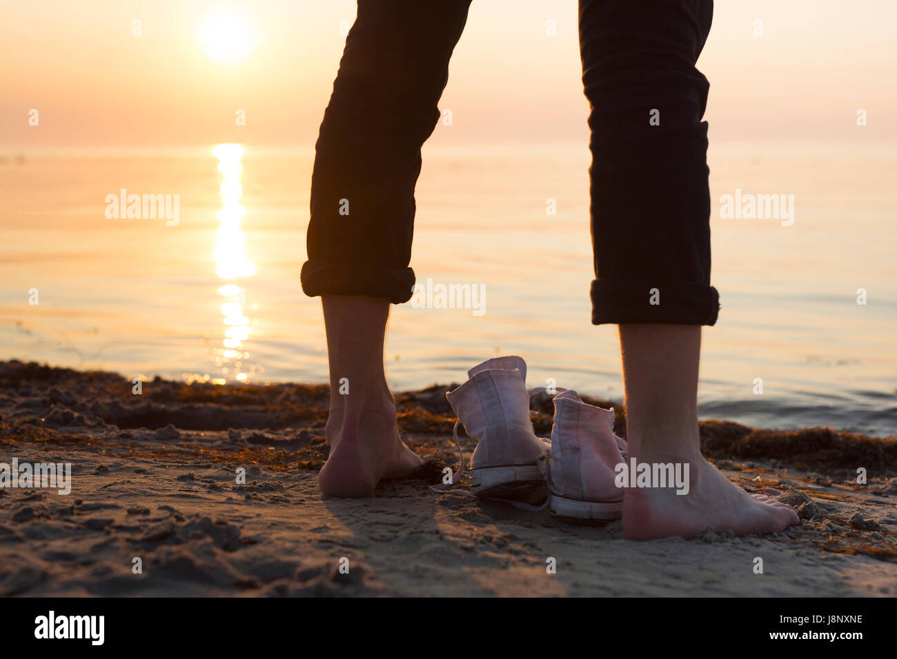 Homme debout par la mer au coucher du soleil Banque D'Images