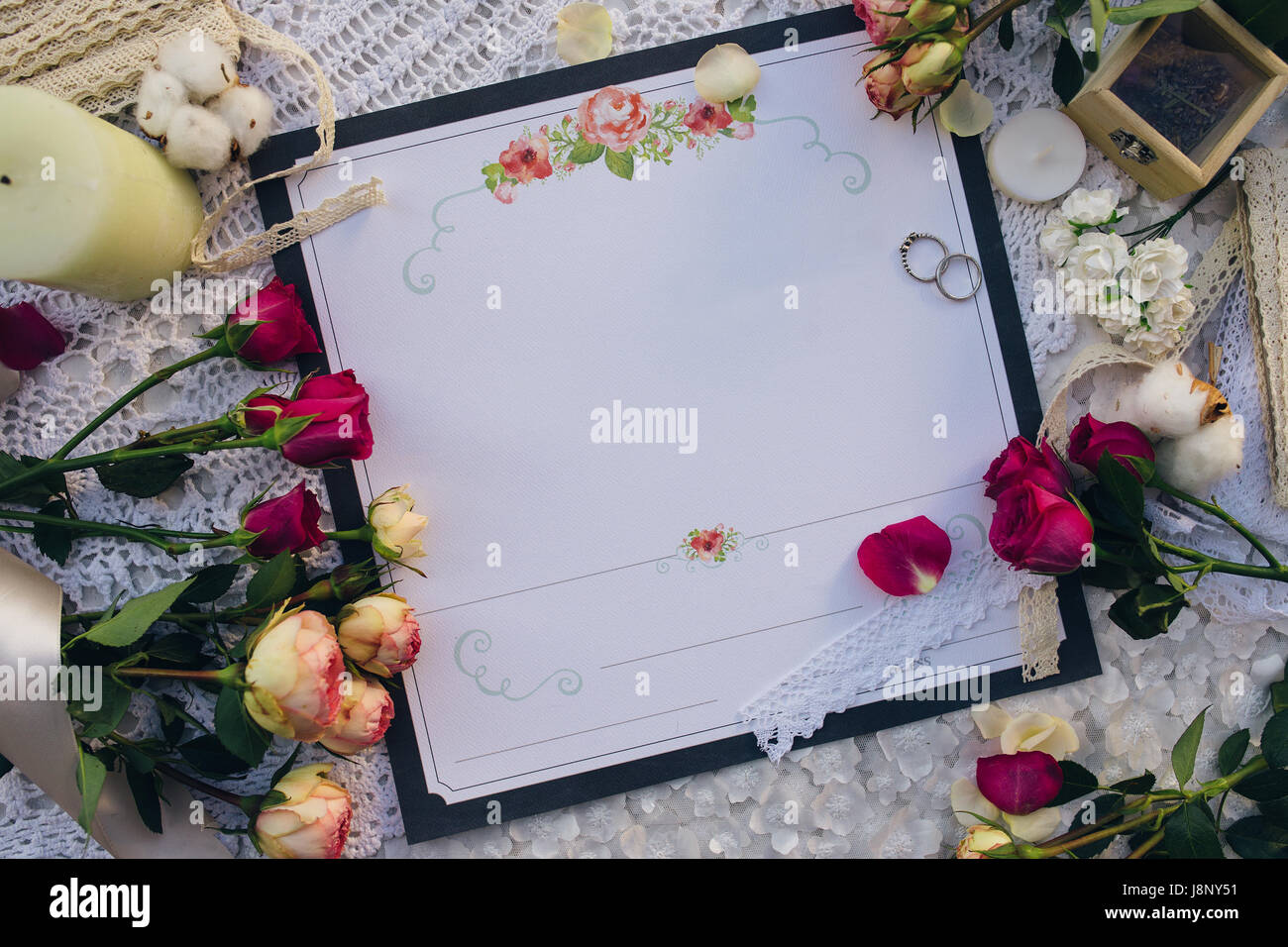 Invitation de mariage, bagues, roses et bougie sur une serviette blanche, vue du dessus Banque D'Images