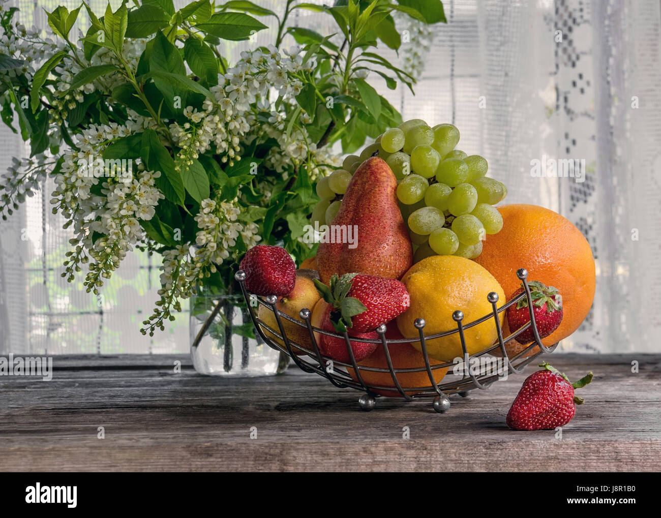 Fruits, poire, pamplemousse, citron, pêche, les fraises sont dans un panier sur le fond d'un bouquet de petites fleurs blanches sur une journée ensoleillée. La structure horizontale. Banque D'Images