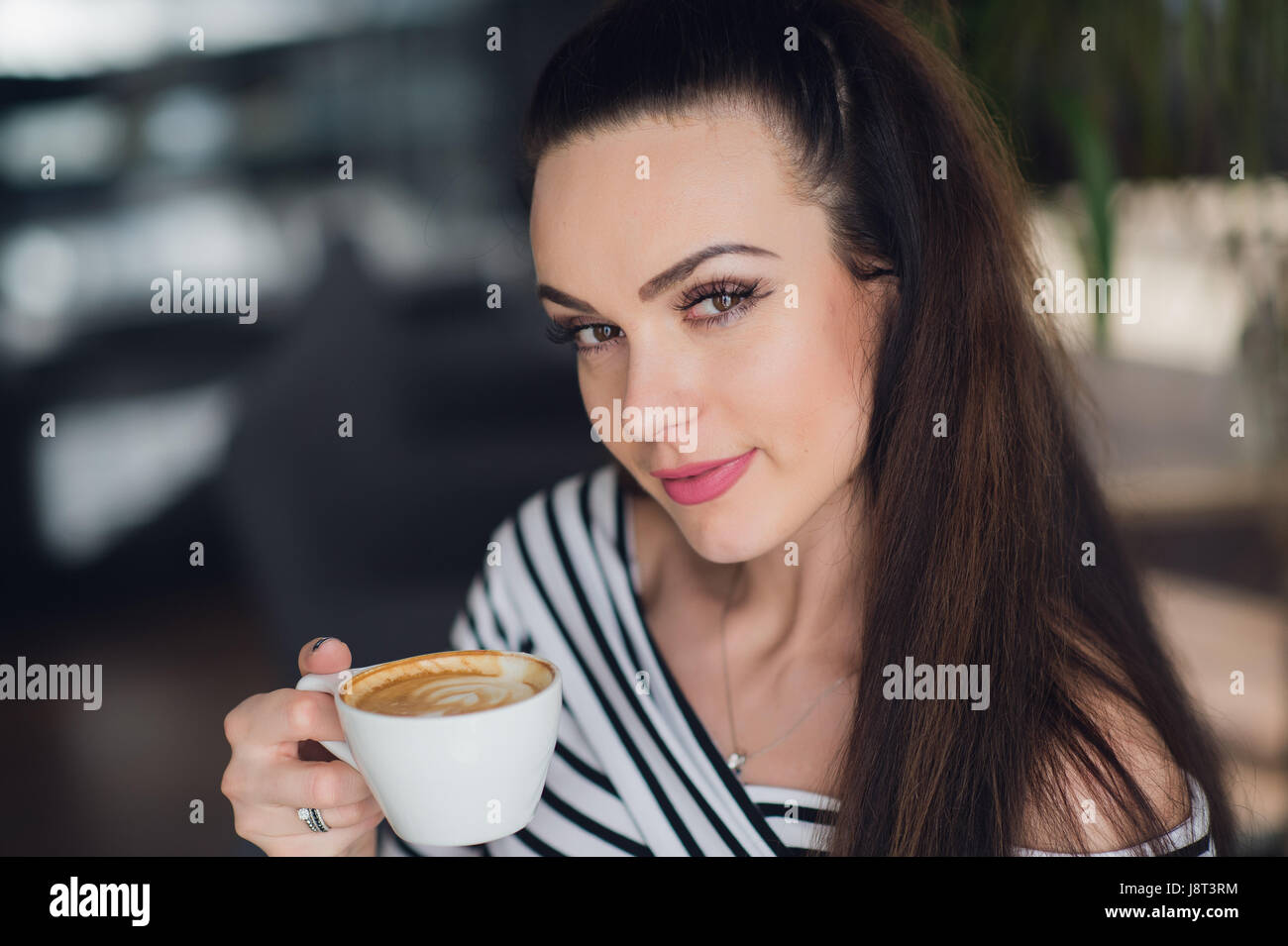 Portrait en gros plan d'une charmante femme tenant une tasse de Cappuccino et regardant la caméra. Banque D'Images