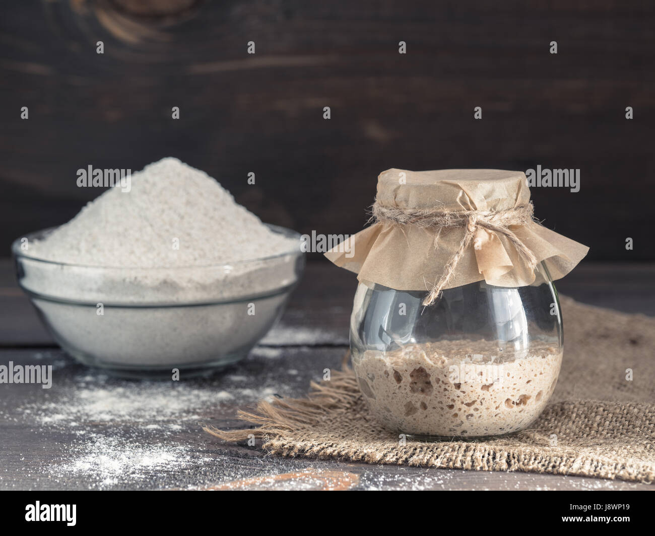 Levain de seigle active du démarreur dans le bocal de verre et la farine de seigle sur fond de bois brun. Démarreur pour pain au levain. La tonalité de l'image. Copier l'espace. Banque D'Images