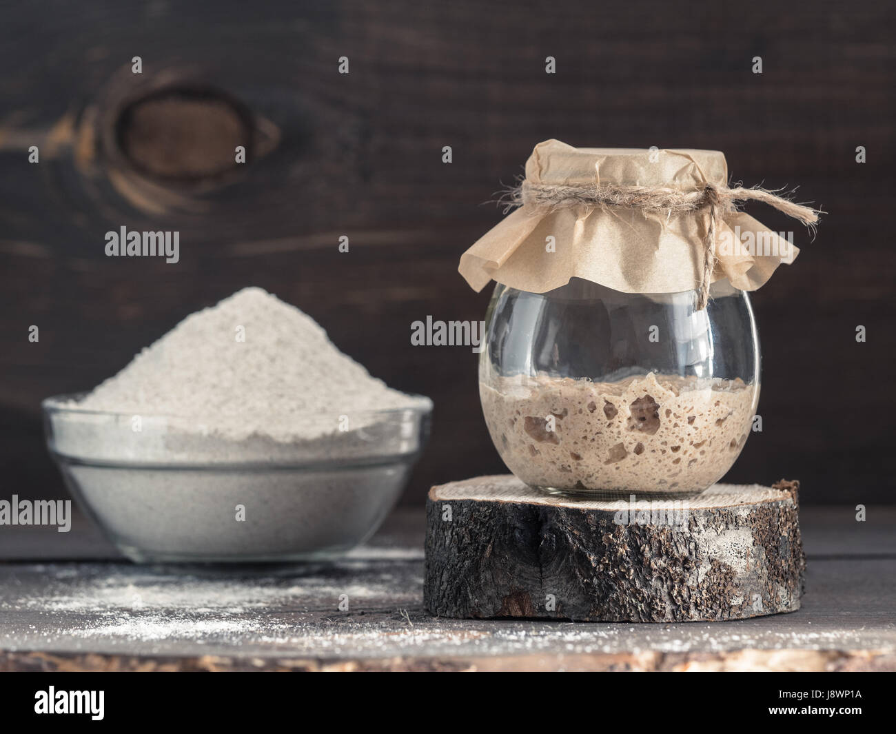 Levain de seigle active du démarreur dans le bocal de verre et la farine de seigle sur fond de bois brun. Démarreur pour pain au levain. La tonalité de l'image. Copier l'espace. Banque D'Images