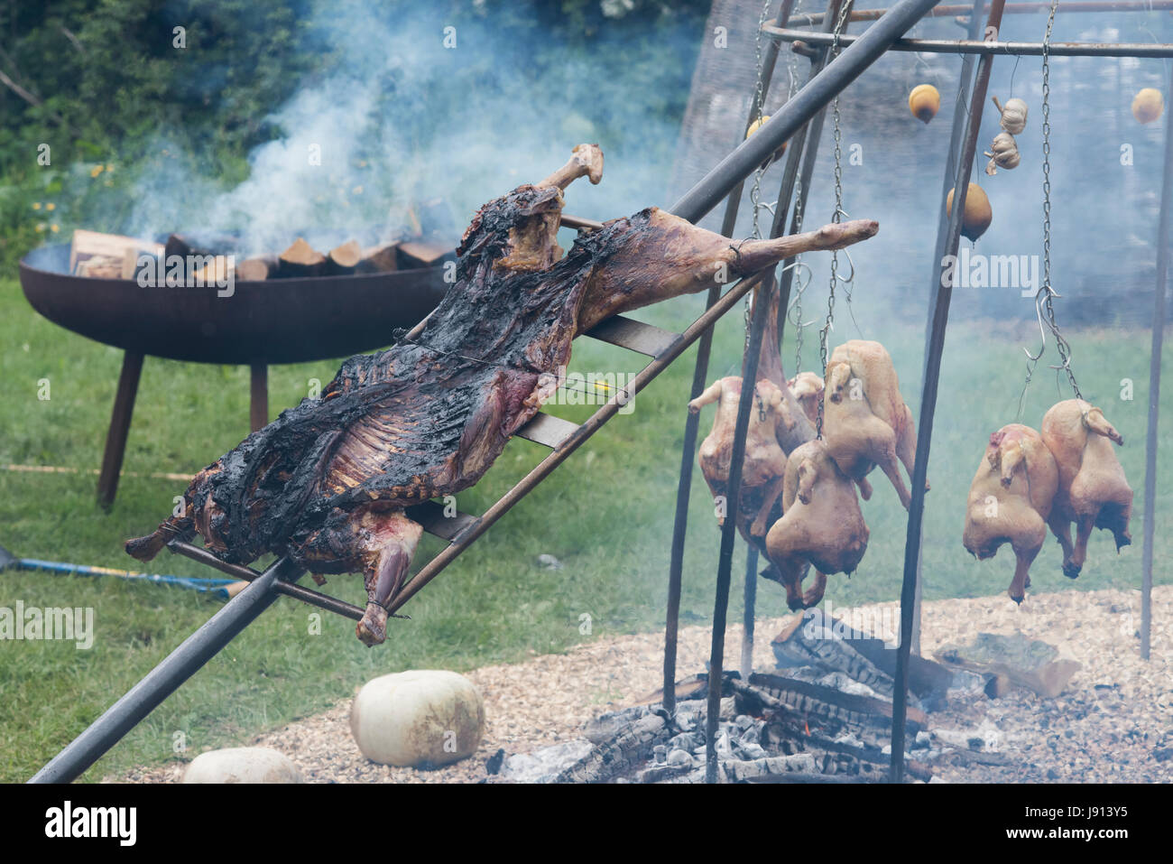 Le feu, à l'Argentine et l'agneau la cuisson des poulets à Daylesford Organic Farm festival d'été. Daylesford, Cotswolds, Gloucestershire, Angleterre Banque D'Images