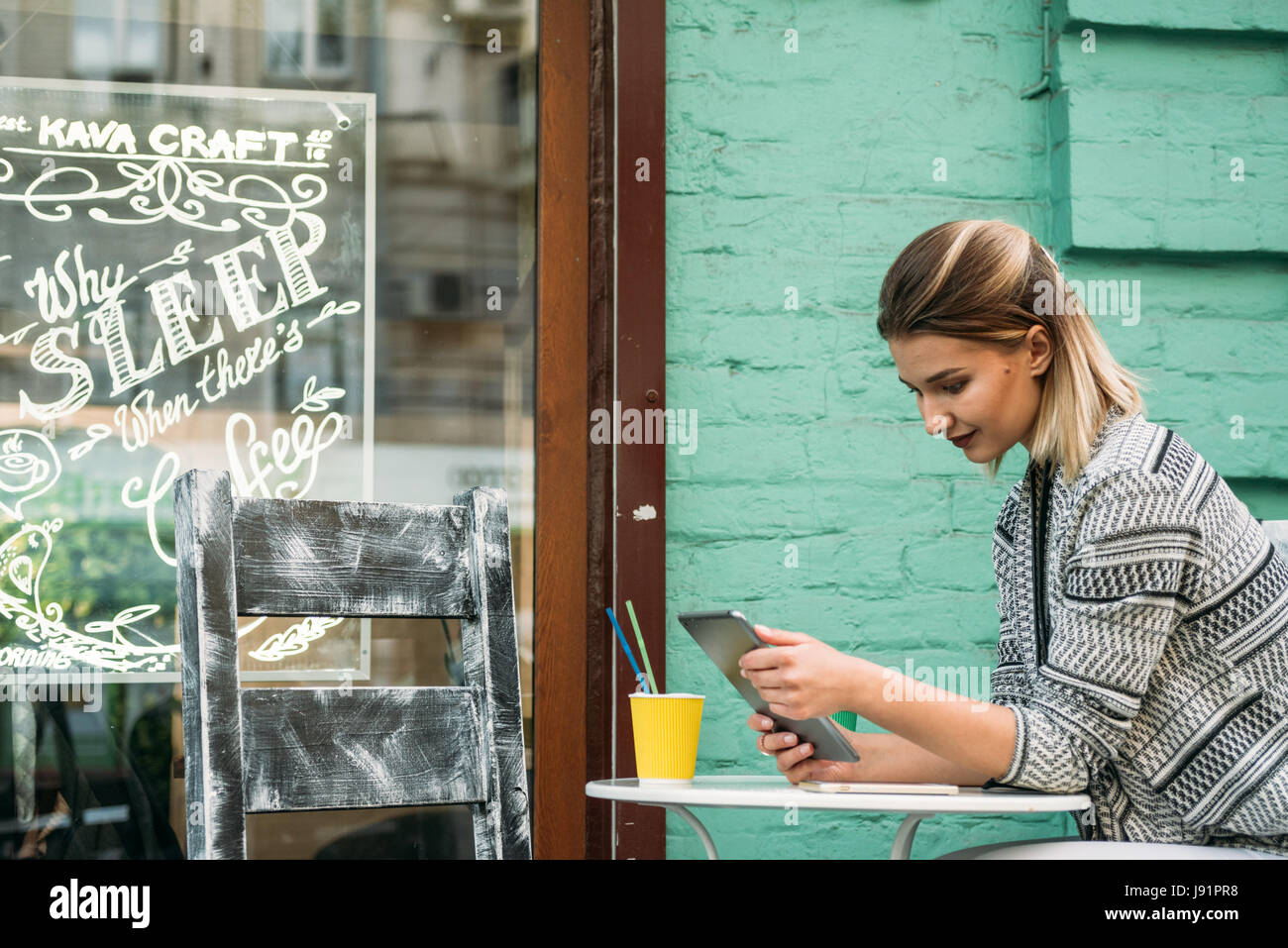 Mode jeune femme boit un cappuccino à l'extérieur d'un café tout en regardant la tablette et en tenant vos autoportraits Banque D'Images