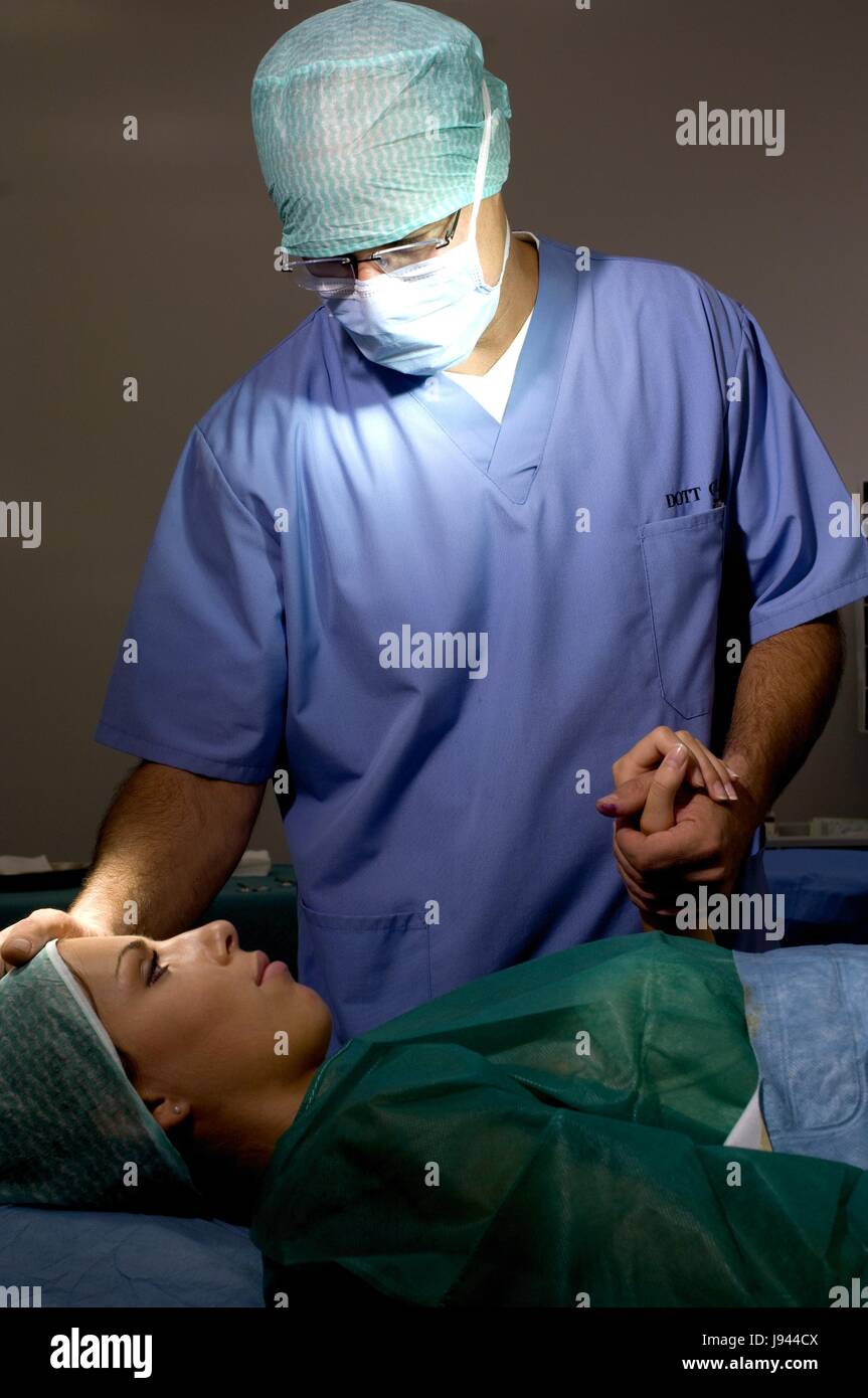 Chirurgien dans la salle d'opération avec un masque chirurgical et surgical cap prépare femme femme patient Banque D'Images
