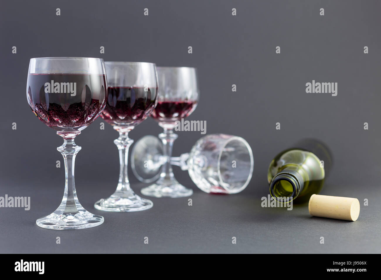 Concept de la consommation d'alcool, l'alcoolisme et l'abus par une ligne de beaux verres de cristal rempli de vin rouge et une bouteille vide. Banque D'Images
