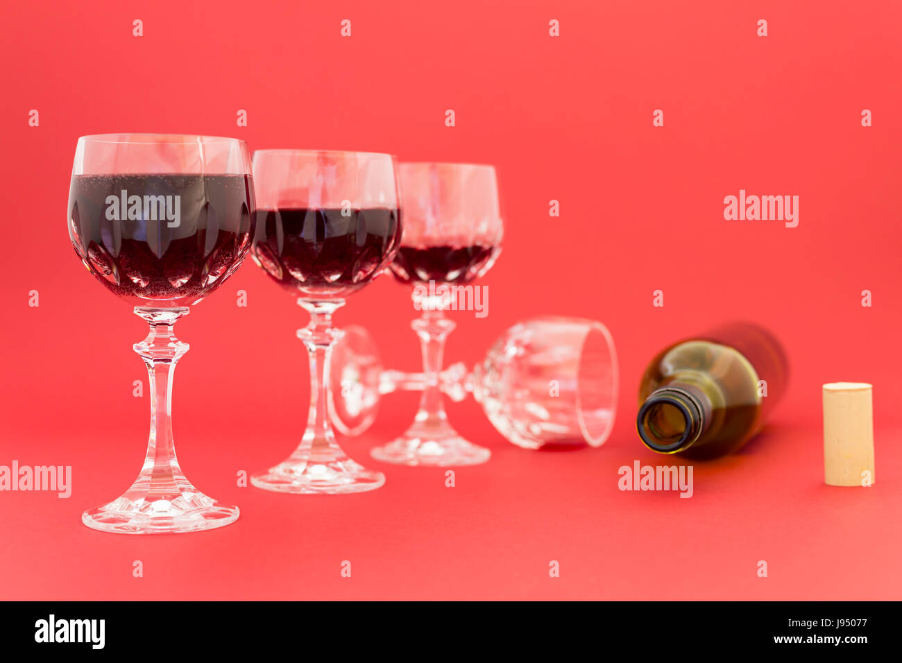 Concept de la consommation d'alcool, l'alcoolisme et l'abus par une ligne de beaux verres de cristal rempli de vin rouge et une bouteille vide. Banque D'Images