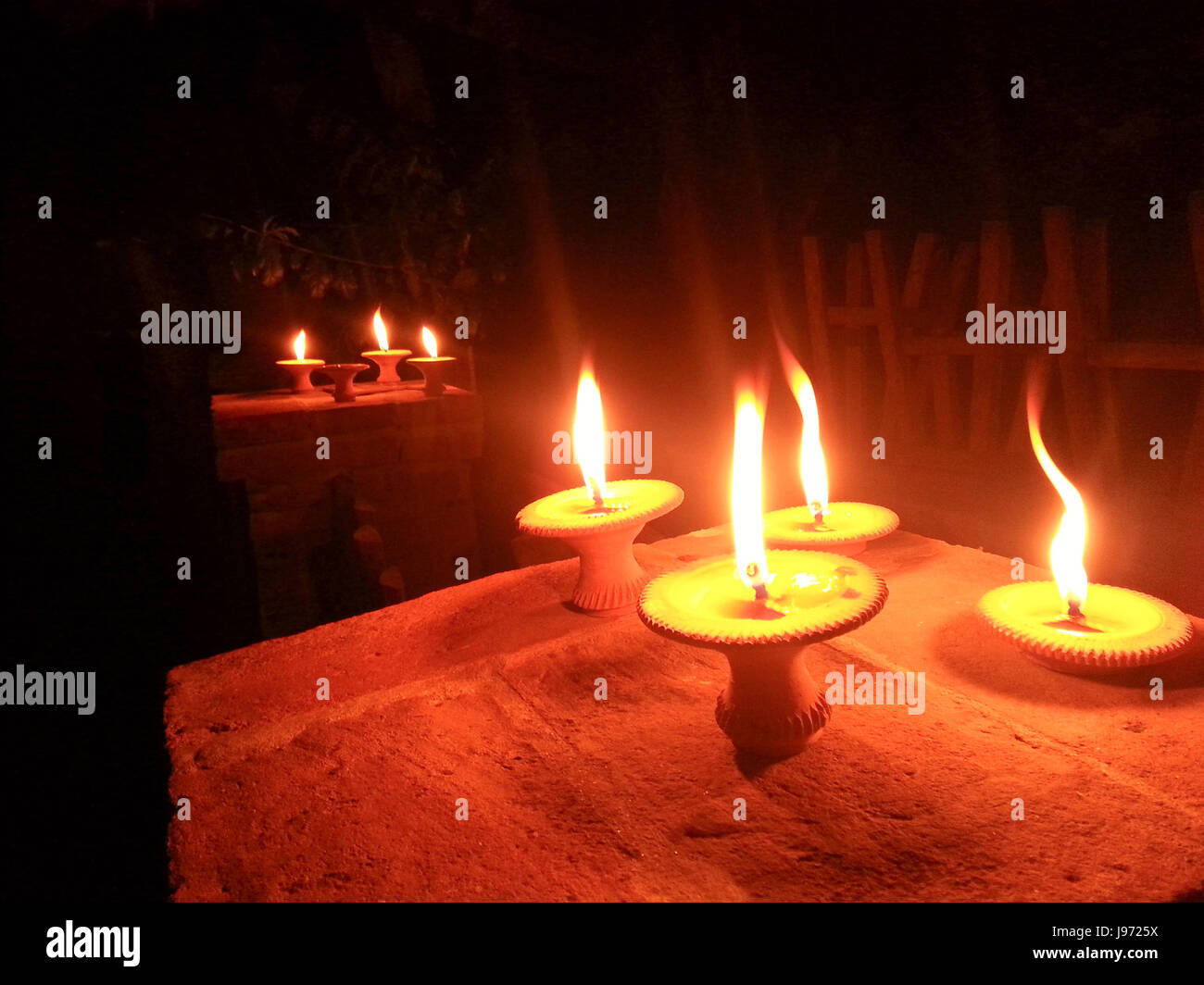La lumière sur la petite flamme de bougie. base de poterie C'est le plancher de bois dans la zone sombre avec abstract bokeh flou fond clair. Banque D'Images