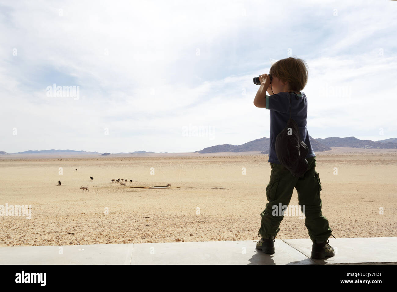 Jeune garçon à la recherche d'esprit un binoculaire à la faune de Garub vue, la Namibie. Banque D'Images