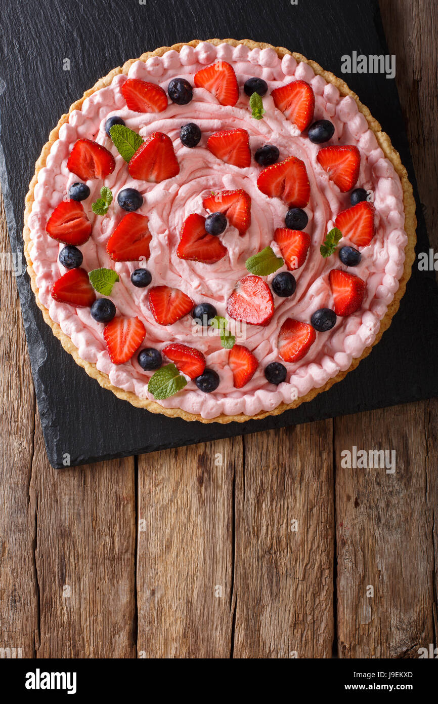 Tarte aux fruits avec de la crème fouettée, fraises et bleuets close-up sur la table. Vue verticale d'en haut Banque D'Images