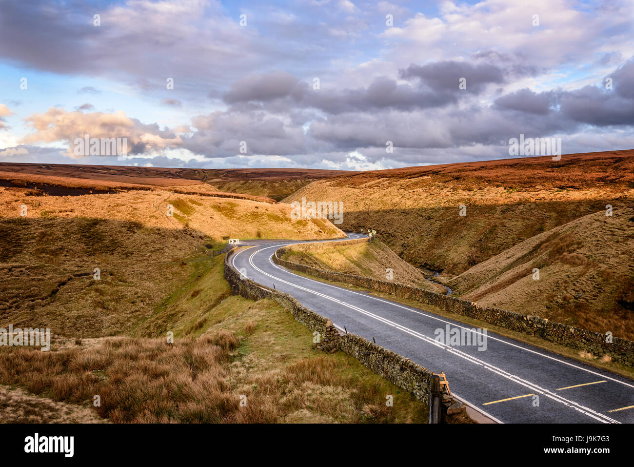 Une route goudronnée serpentant à travers la lande sur un jour nuageux dans la région de Peak District, l'Angleterre. Banque D'Images