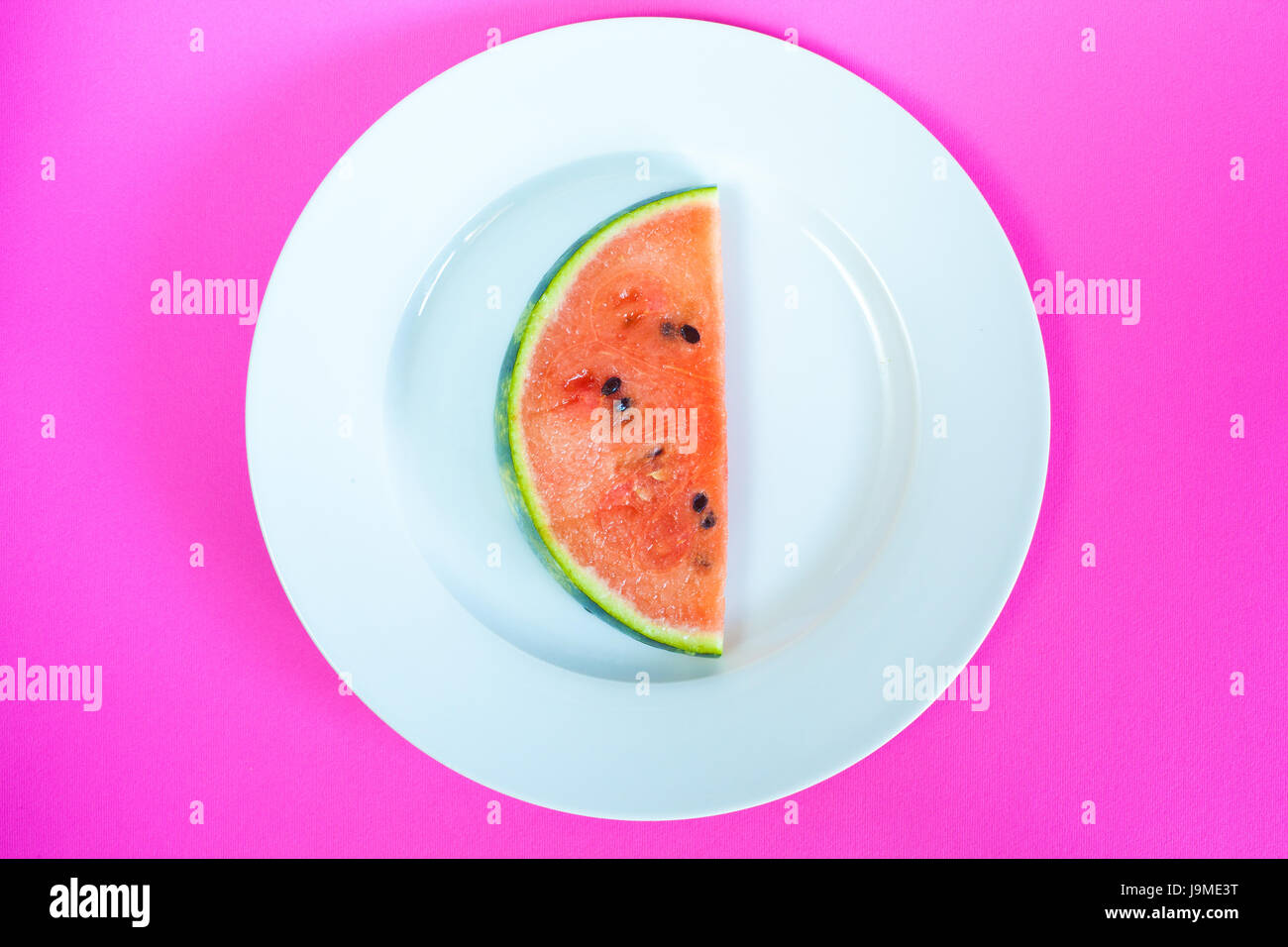 Watermelon slice servi sur une assiette blanche avec fond violet. Banque D'Images