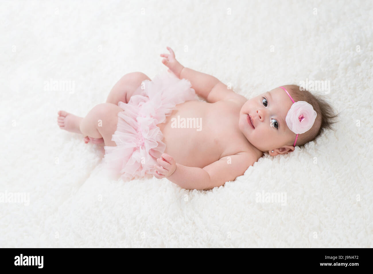 Portrait d'un bébé de quatre mois girl wearing frilly, rose et une fleur rose, serre-tête. Tourné en studio sur une couverture blanche. Banque D'Images