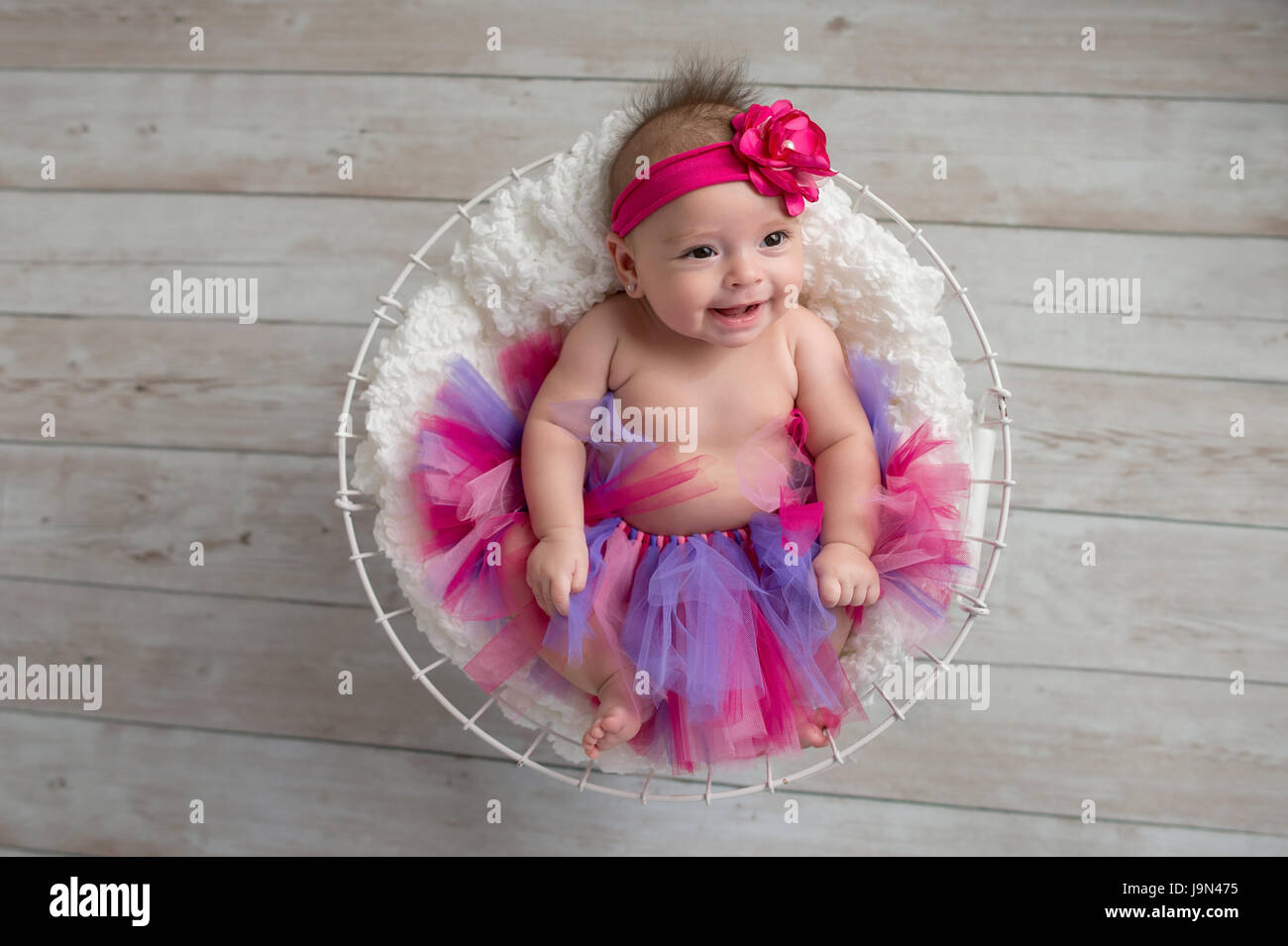 Portrait of a smiling, quatre mois, bébé fille couchée dans un panier métallique et le port, rose à froufrous rose et une culotte, fleur serre-tête. Banque D'Images