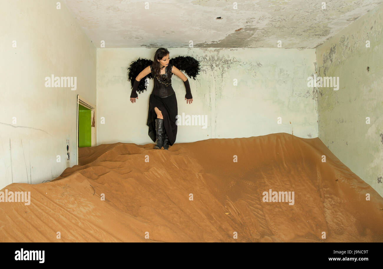 Jeune femme se reposant à l'intérieur d'une maison qui a été supplanté par le sable Banque D'Images