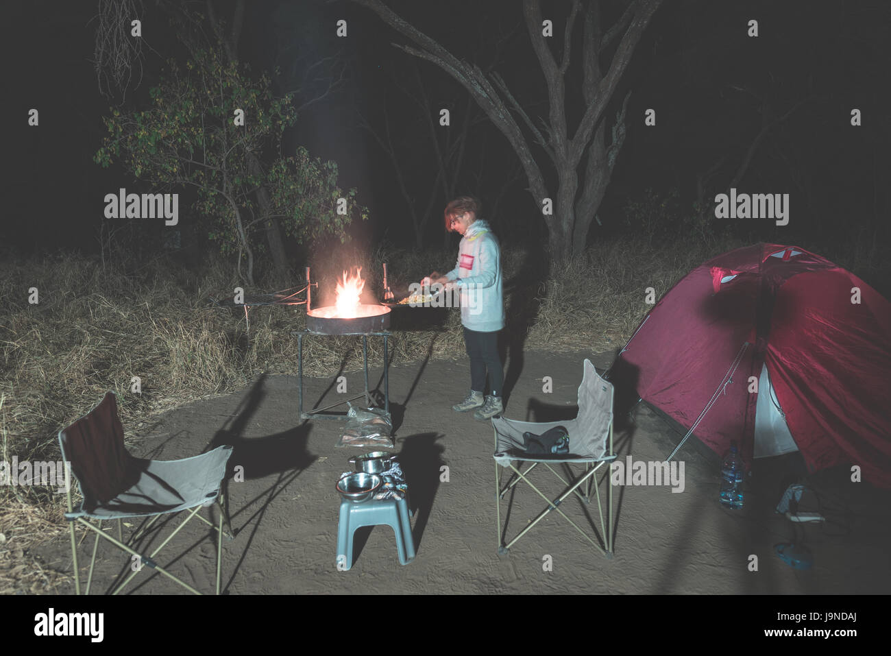 La cuisson au feu de bois avec femme et braai matériel par nuit. Tente et des chaises au premier plan. Aventures dans les parcs nationaux d'Afrique. La tonalité de l'image. Banque D'Images