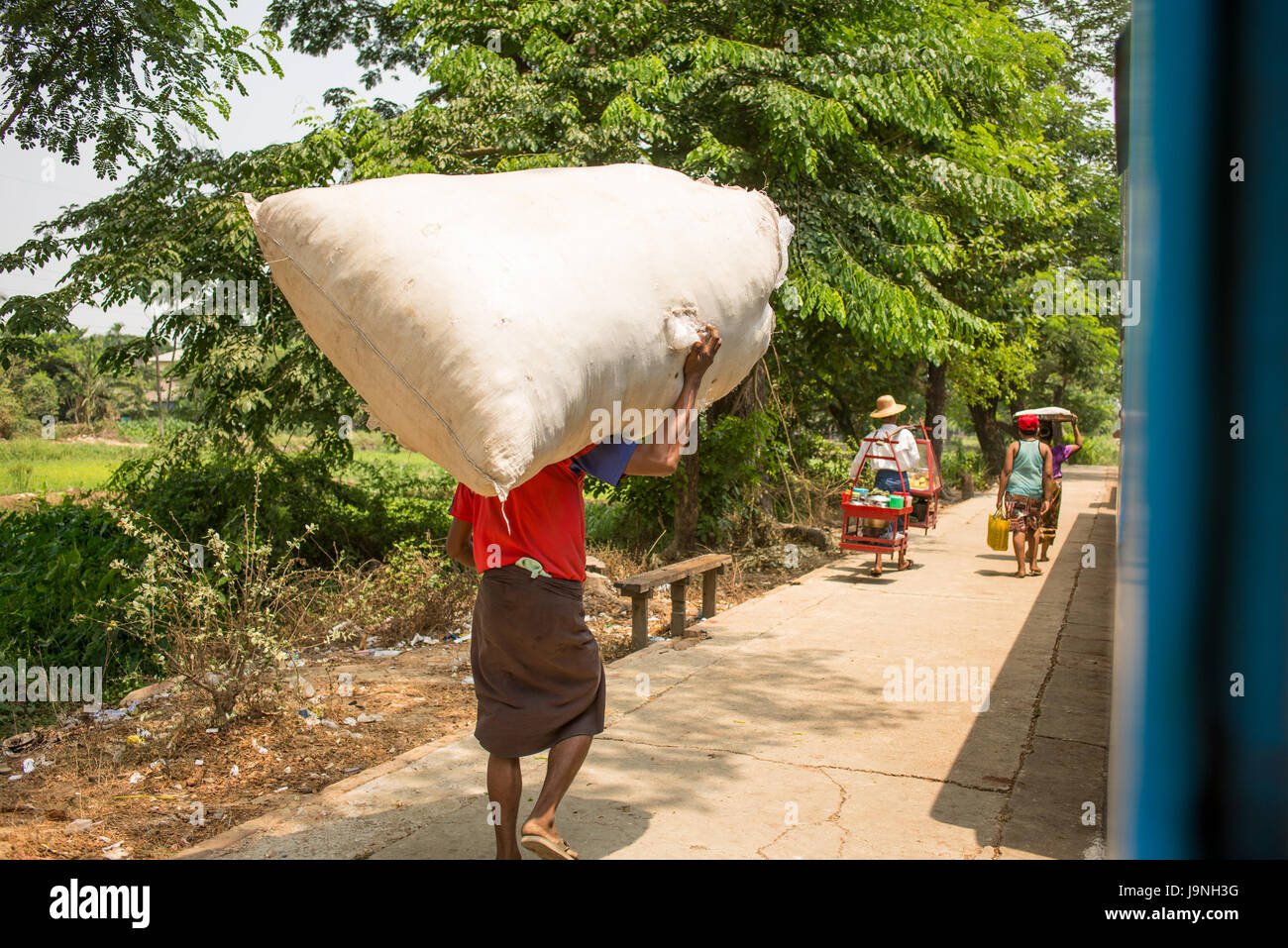 Un homme porte un grand sac blanc sur la plate-forme sur le chemin de fer circulaire de Yangon. Yangon, Myanmar. Banque D'Images