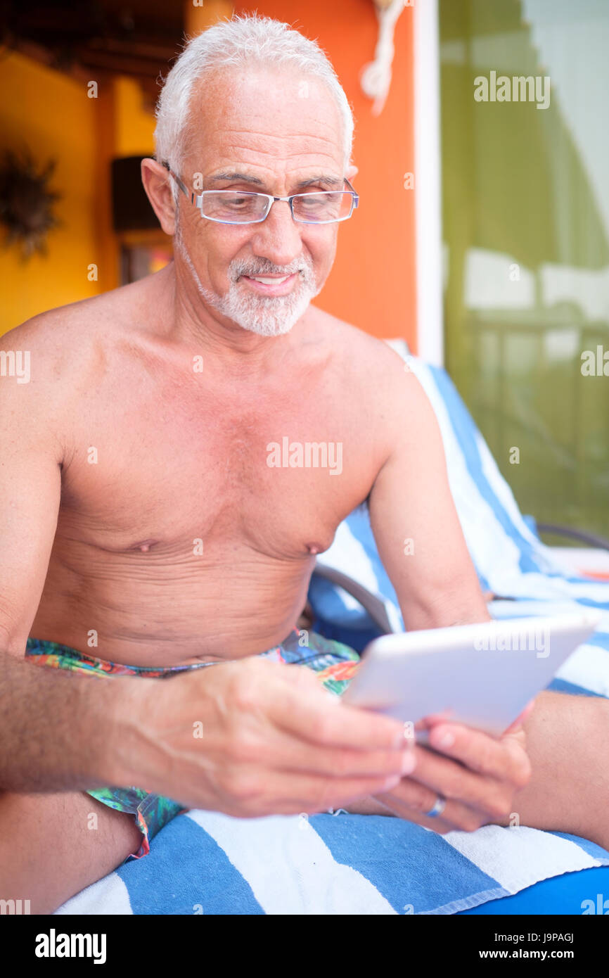 Homme plus âgé d'environ 60 à l'aide de l'ordinateur tablette pour lire en vacances Banque D'Images