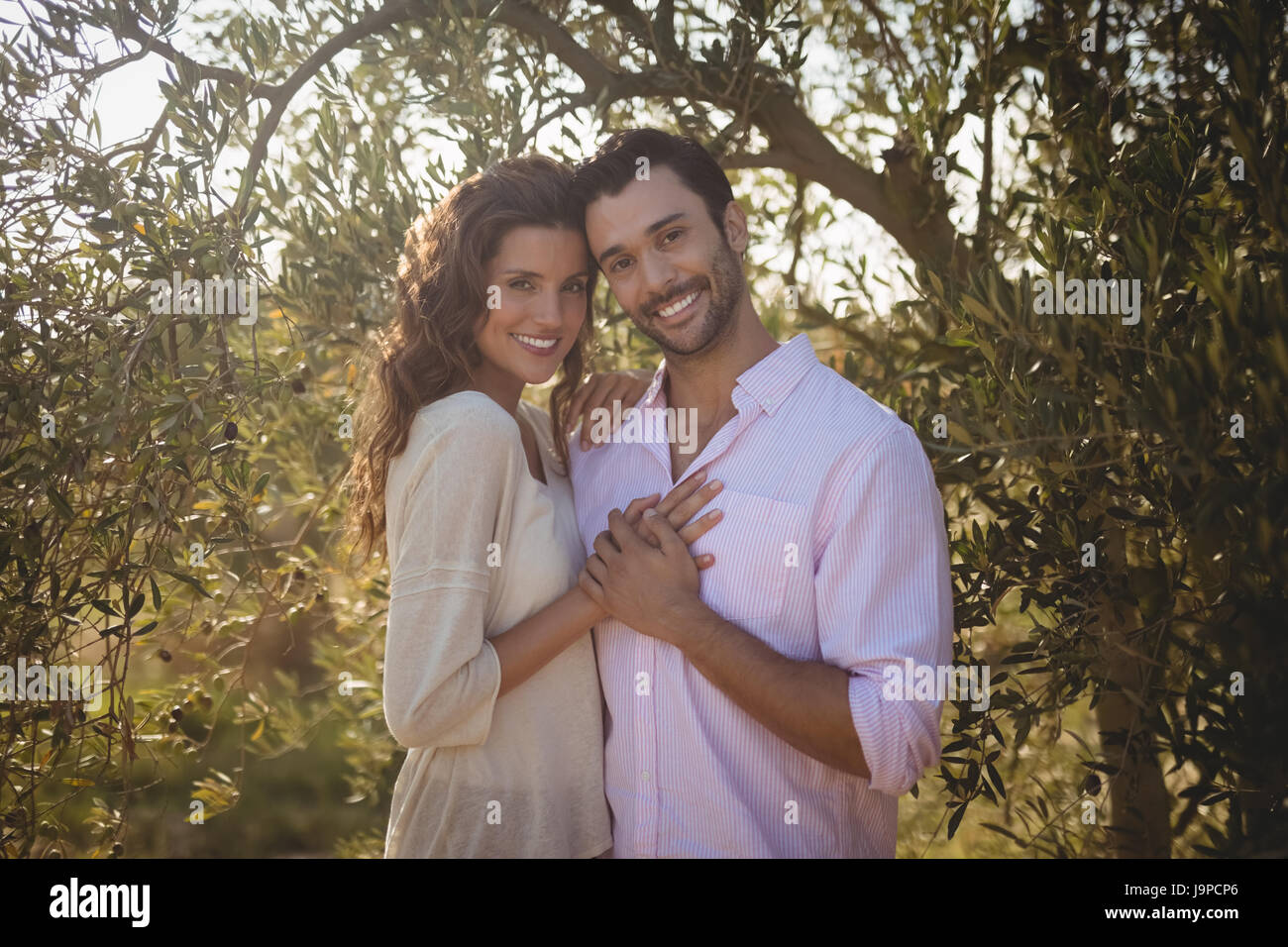 Portrait of smiling young couple embracing par arbre à la ferme d'olive Banque D'Images