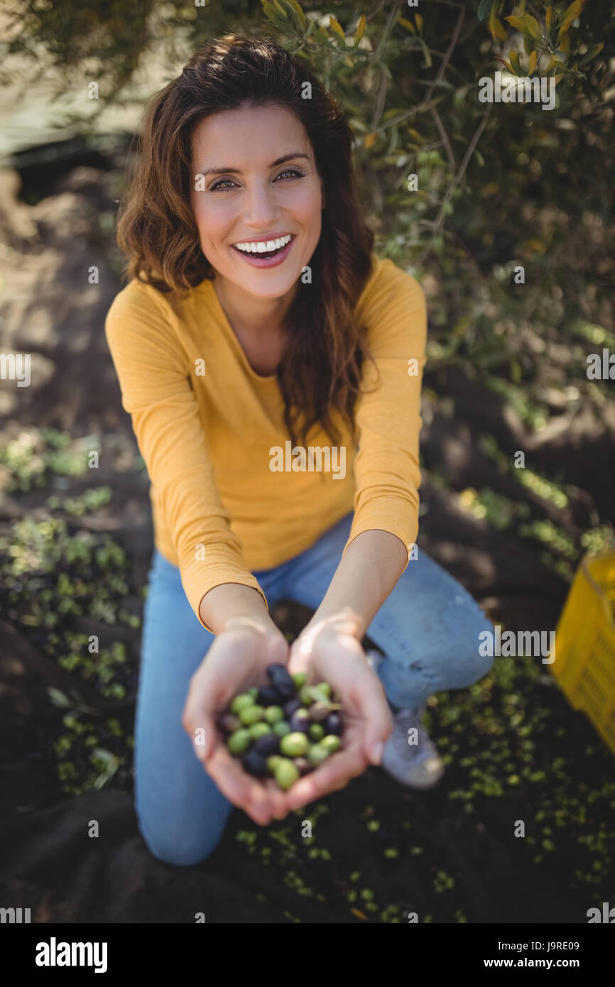 Portrait of smiling woman showing olives alors que accroupi sur le champ à farm Banque D'Images