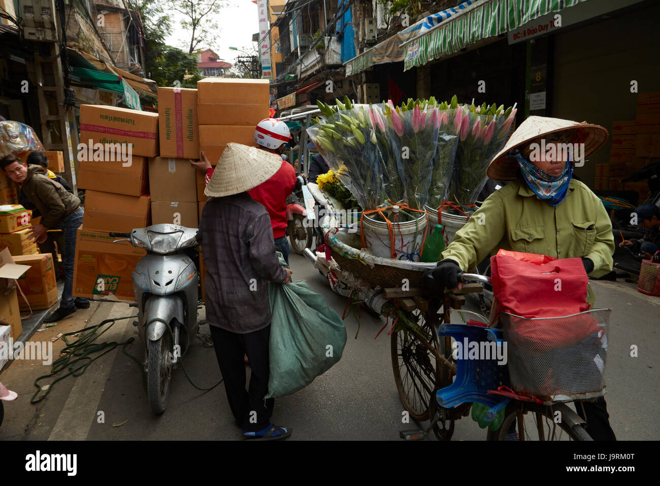 Femme avec des fleurs et de scooters surchargés de boîtes, vieux quartier, Hanoi, Vietnam Banque D'Images
