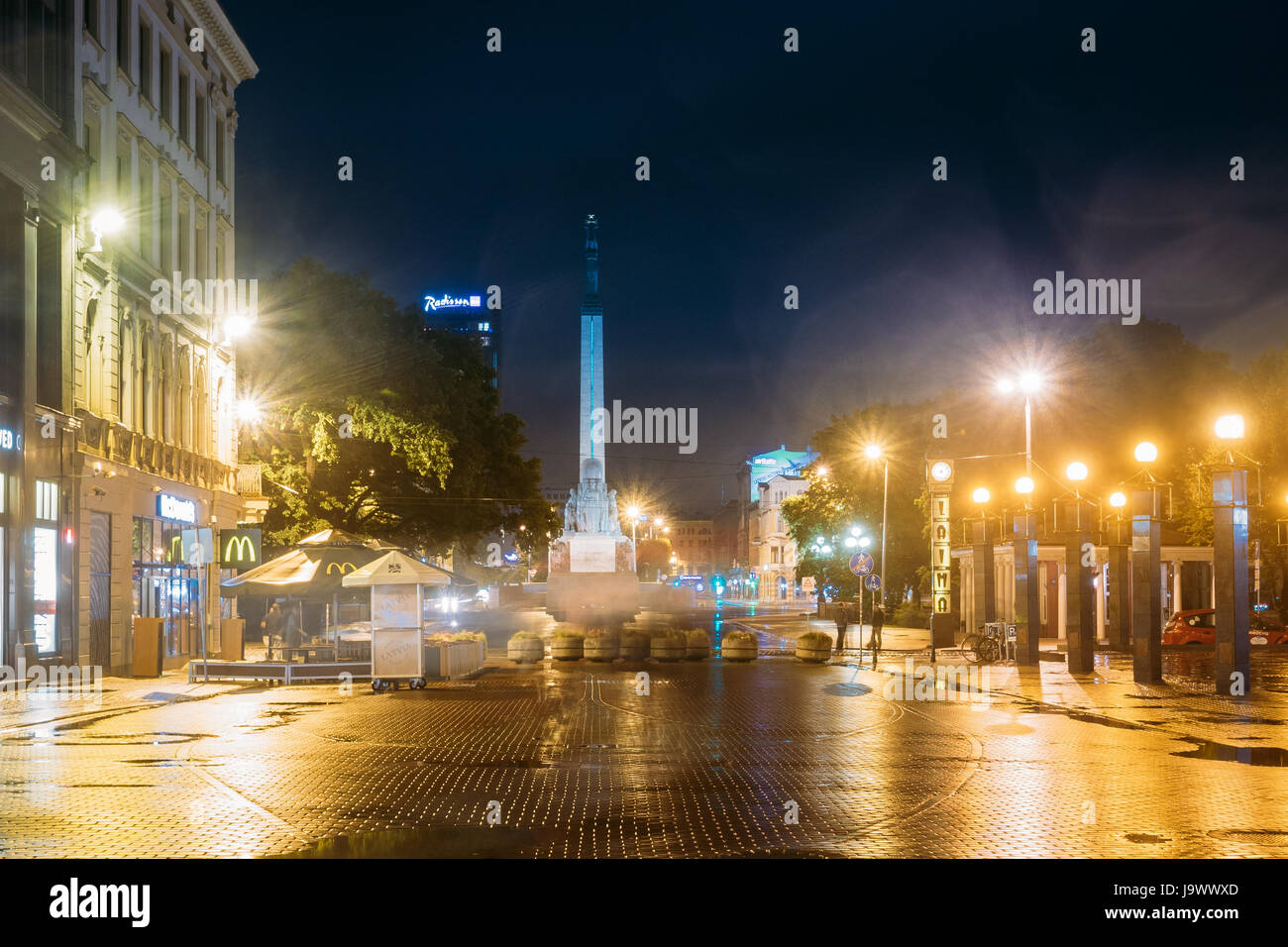 Riga, Lettonie - 4 juillet 2016 : Night View Of Memorial Monument de la liberté à la place de la liberté et l'horloge Laima éclairage dans l'éclairage de nuit. Vue depuis Kalku Banque D'Images