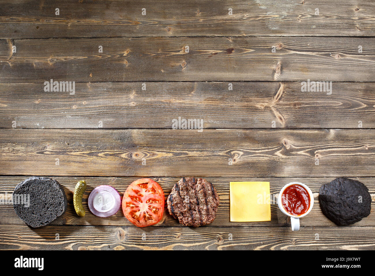 Ingrédients pour la cuisson burger noir. La viande grillée patty, brioches, oignons, tomates, laitue, cornichons, sauce, fromage sur fond de bois noir Vue de dessus Banque D'Images