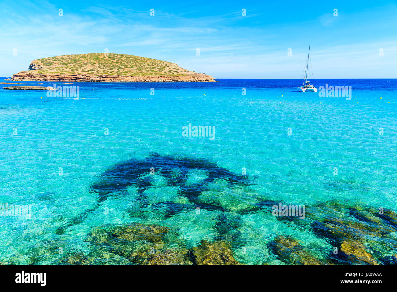 L'eau turquoise de la baie de Cala Comte et voile voile sur mer en arrière-plan, l'île d'Ibiza, Espagne Banque D'Images