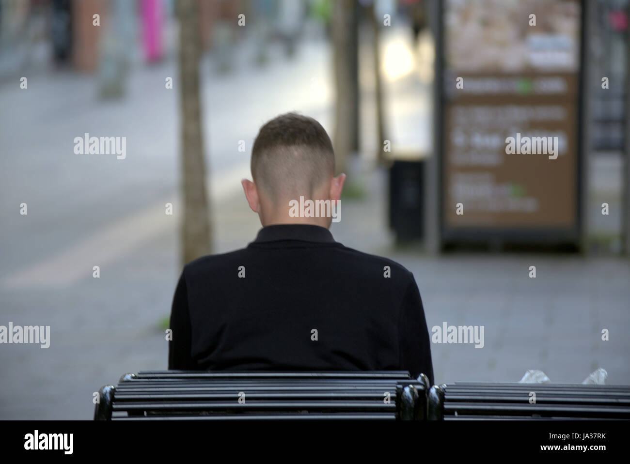 Jeune personne assise sur un banc les oreilles vu de derrière Banque D'Images