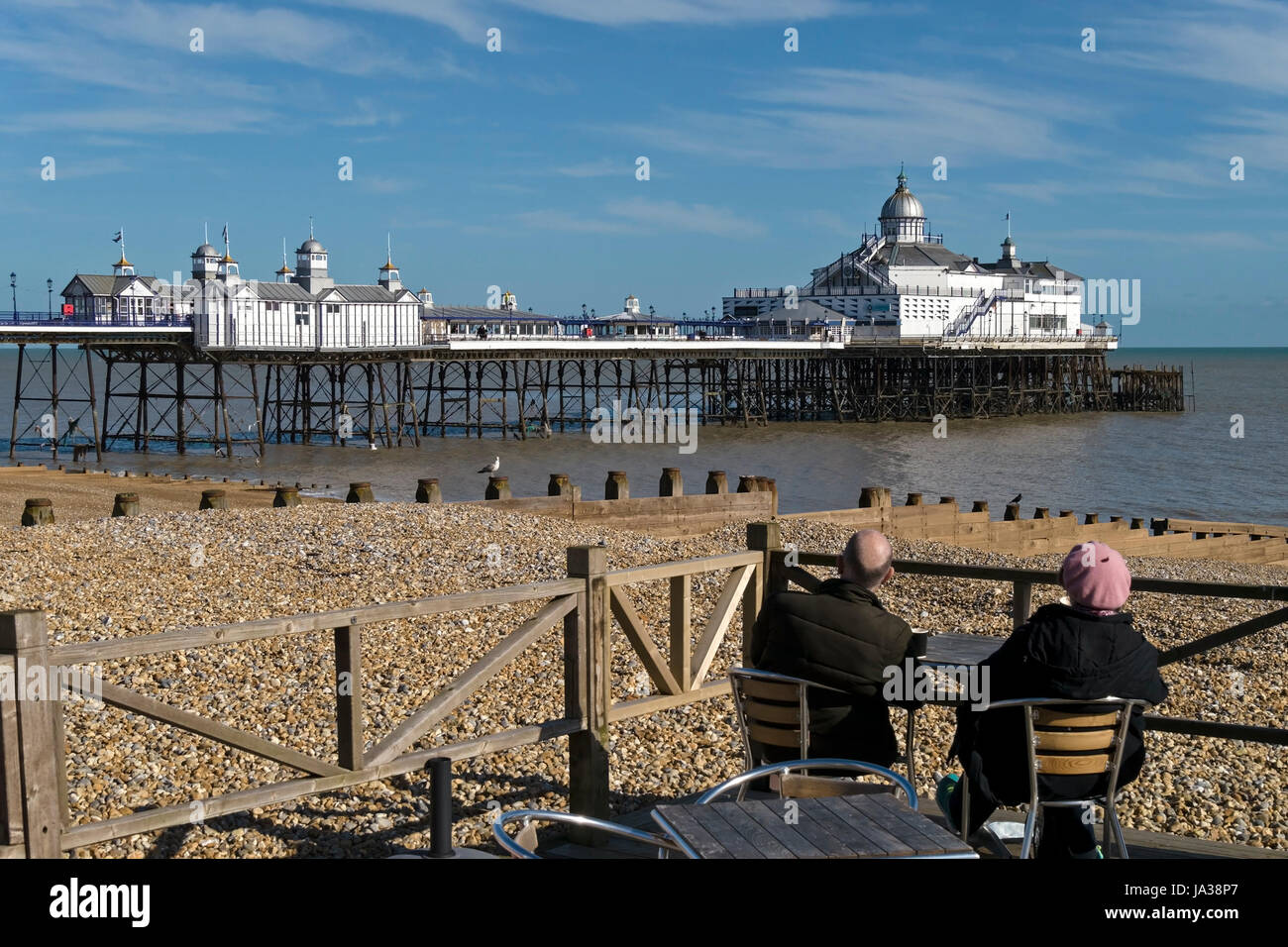 Assis couple admiring view de la jetée d''Eastbourne avec plage de galets en premier plan, East Sussex, England, UK Banque D'Images