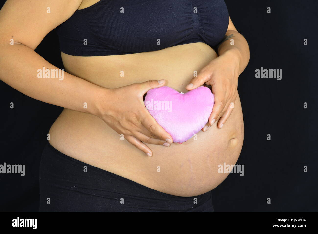 Une femme enceinte tenant une lumière sunglasses contre son abdomen. Banque D'Images