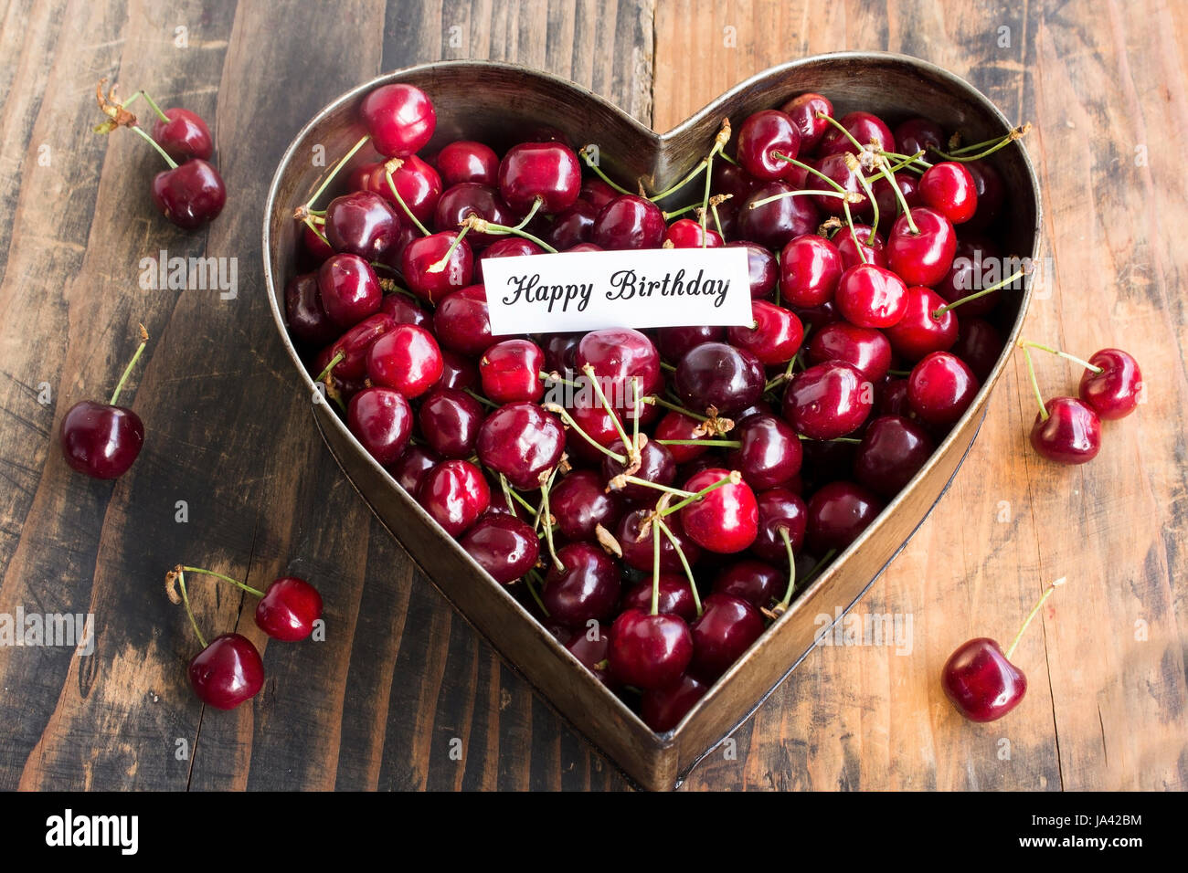Joyeux anniversaire carte avec les cerises au coeur moule à gâteaux sur un fond de bois rustique. Banque D'Images