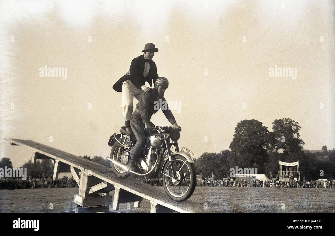 Années 1950, historiques, clown est sur le siège d'une moto sur une holding le pilote comme il tombe sur une rampe en bois, England, UK. Banque D'Images
