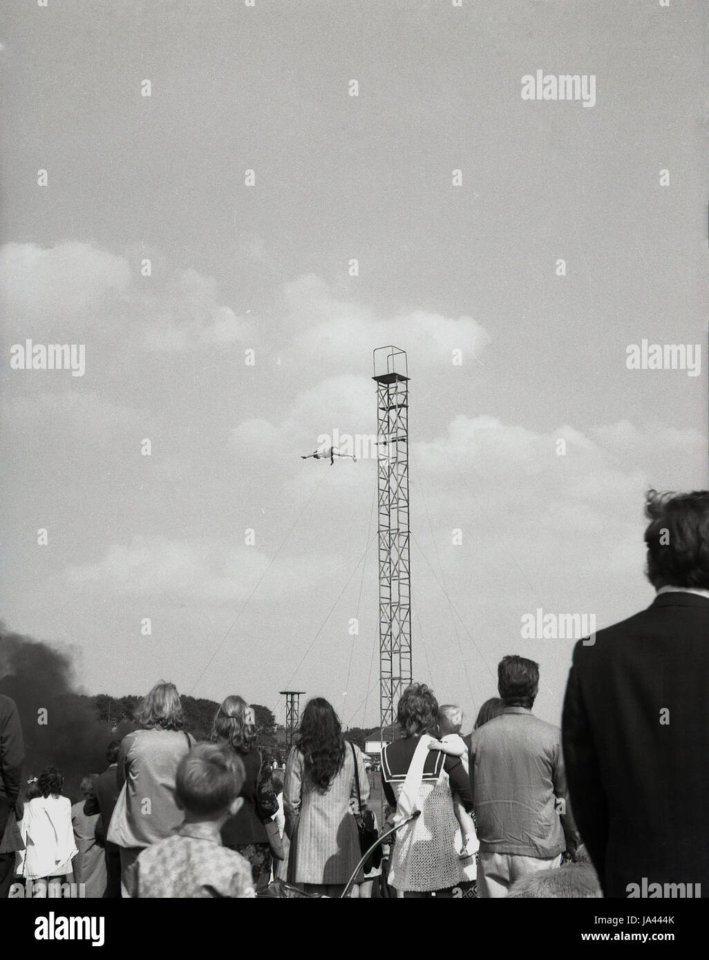 Des années 1970, l'Angleterre, foule regarder comme un homme plonge d'un acier haute tour à une fête foraine. Banque D'Images