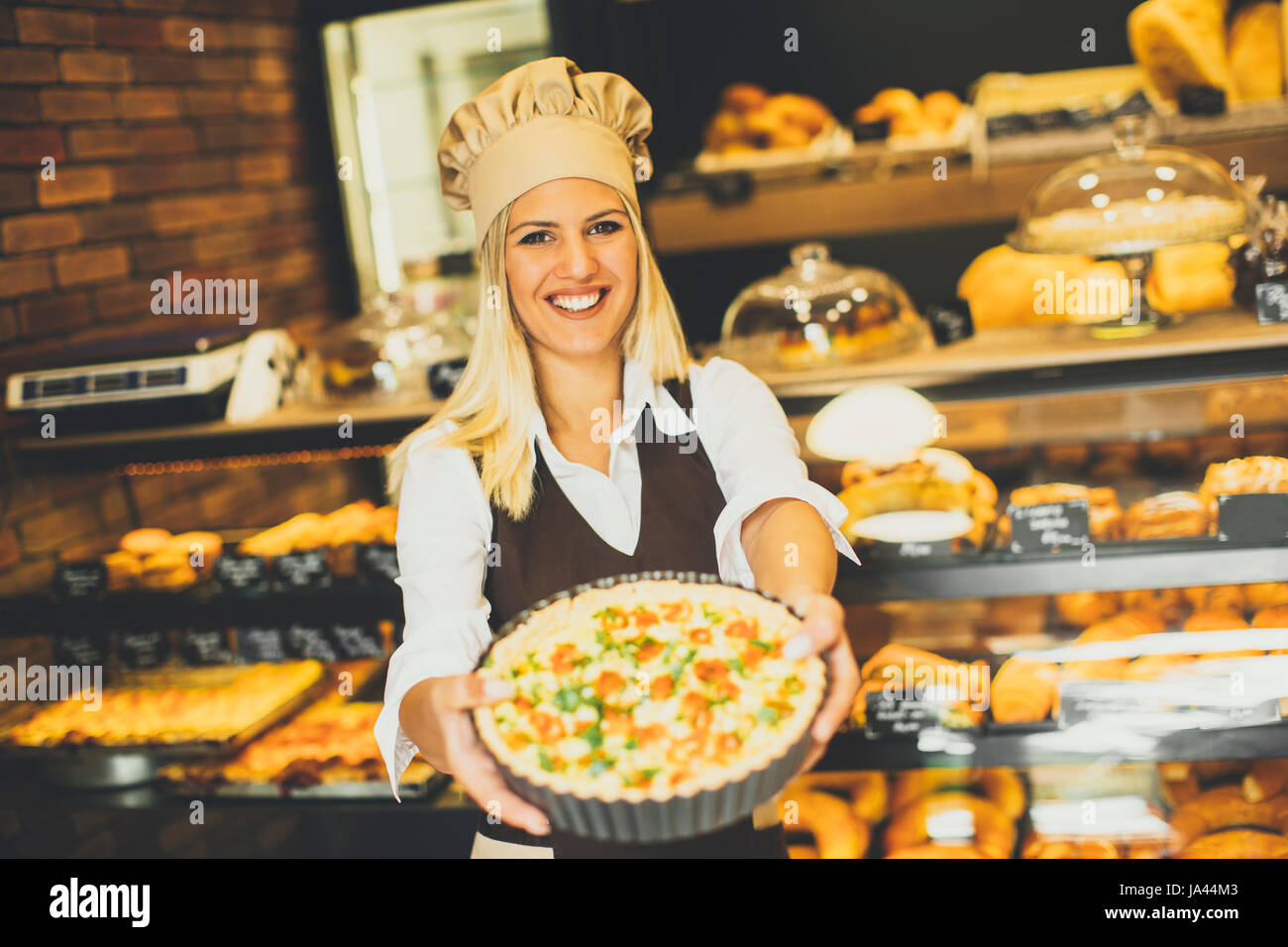 Jeune femme baker debout dans la boulangerie et pizza montre Banque D'Images