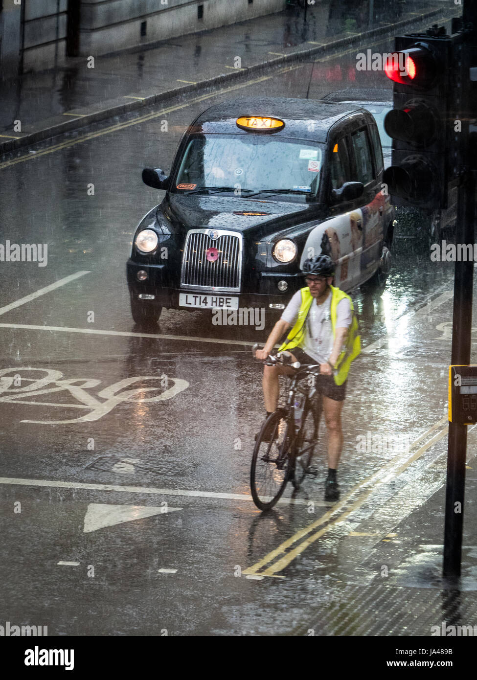 London Cyclist & London taxi Black Cab attendez aux feux de signalisation pendant les fortes pluies dans le centre de Londres, au Royaume-Uni Banque D'Images