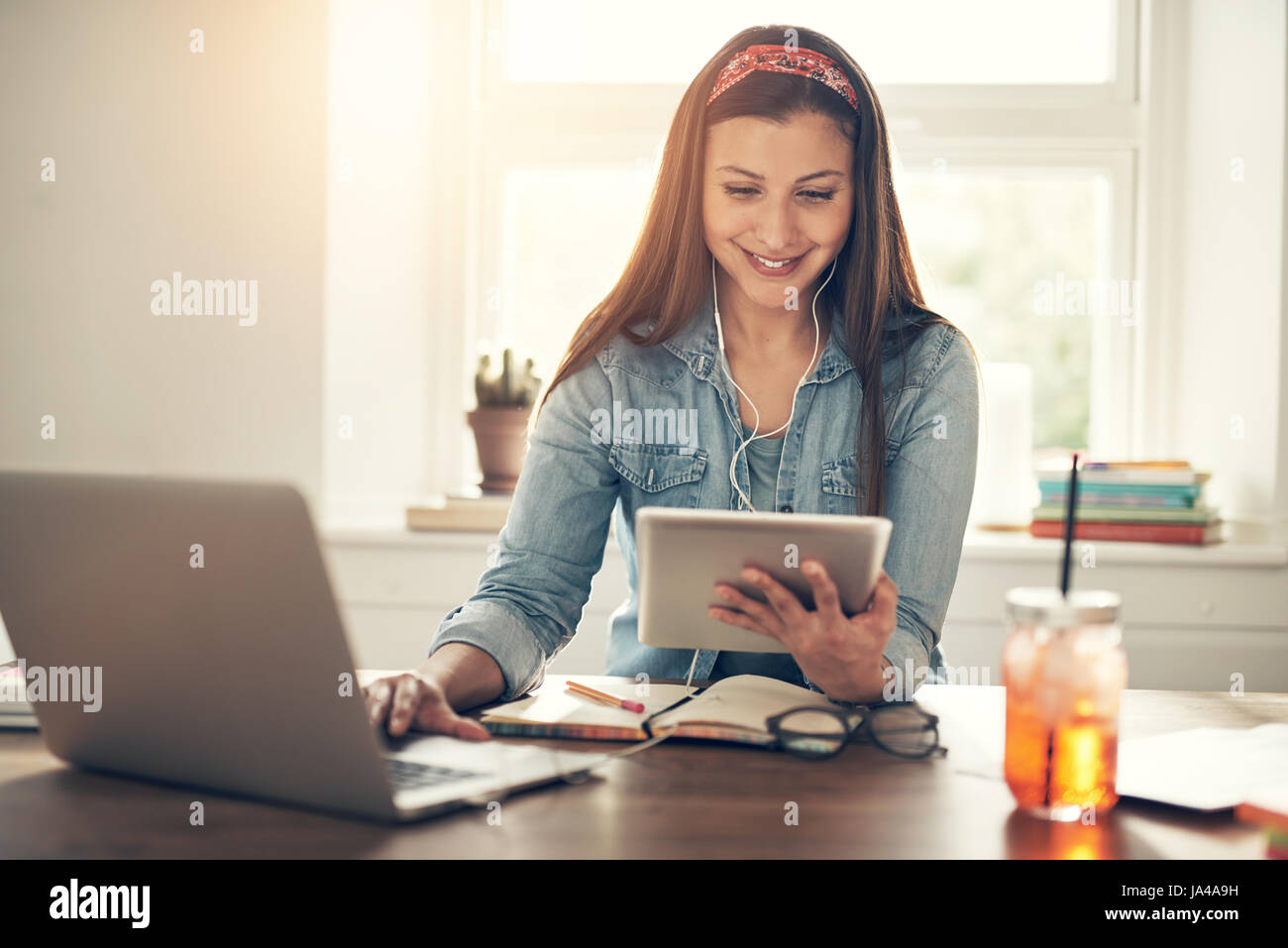 Cheerful young femme entrepreneur parcourt tablet pc portable et des écouteurs au lieu de travail en bureau. Banque D'Images