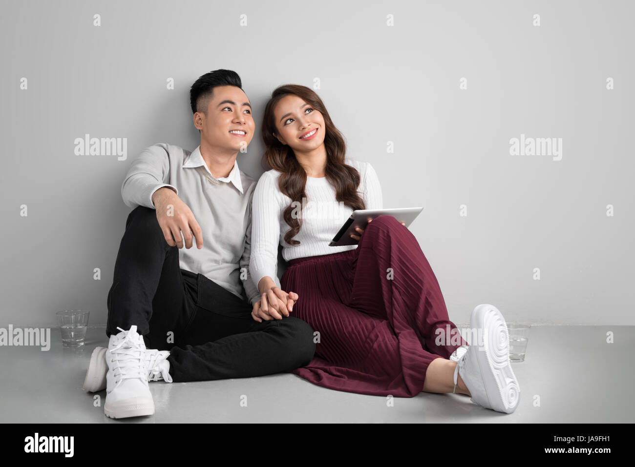 Pretty smiling asian couple dans l'amour ensemble assis sur le plancher bénéficiant using digital tablet Banque D'Images