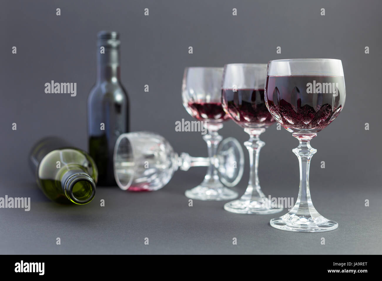 Concept de la consommation d'alcool, l'alcoolisme et l'abus par une ligne de beaux verres de cristal rempli de vin rouge, un plein et une bouteille vide. Étapes Banque D'Images