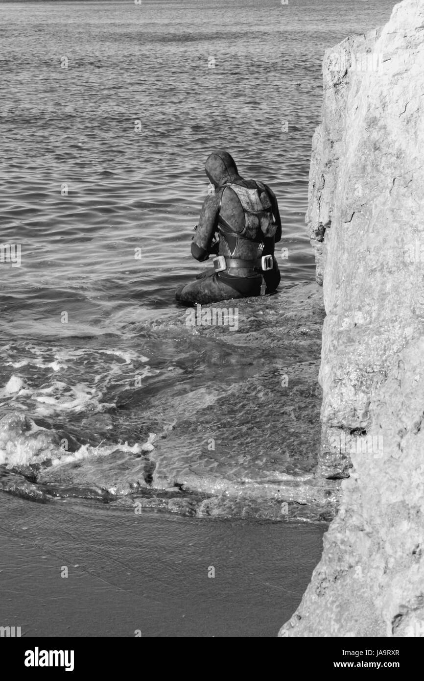 Scuba Diver assis sur la roche est sur le point d'entrer dans l'eau Banque D'Images