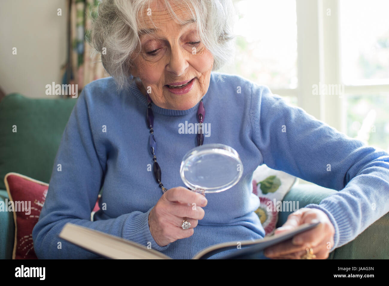 Senior Woman Reading Book à l'aide de Loupe Banque D'Images