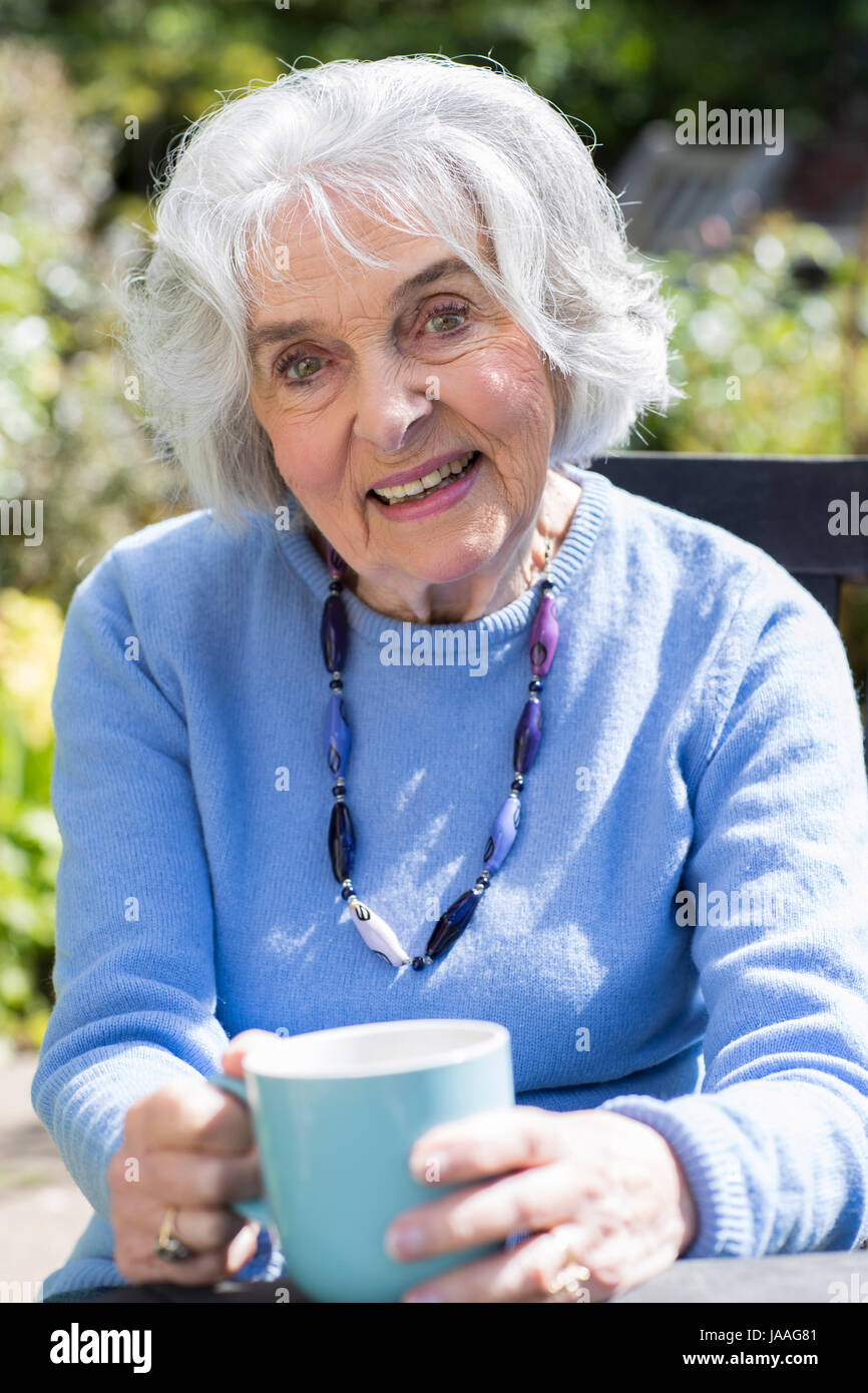 Portrait of Senior Woman Relaxing In Jardin avec boisson chaude Banque D'Images