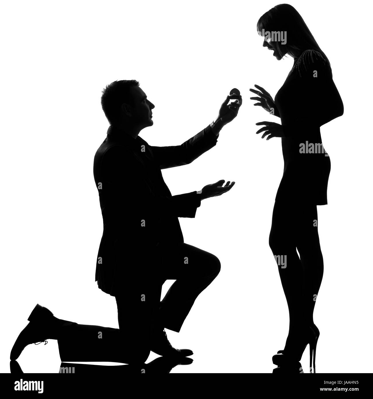 Un couple homme à genoux offrant une bague de fiançailles et femme heureuse surprise en silhouette studio isolé sur fond blanc Banque D'Images Un couple homme à genoux offrant une bague de fiançailles et femme heureuse surprise en silhouette studio isolé sur fond blanc Banque D'Images