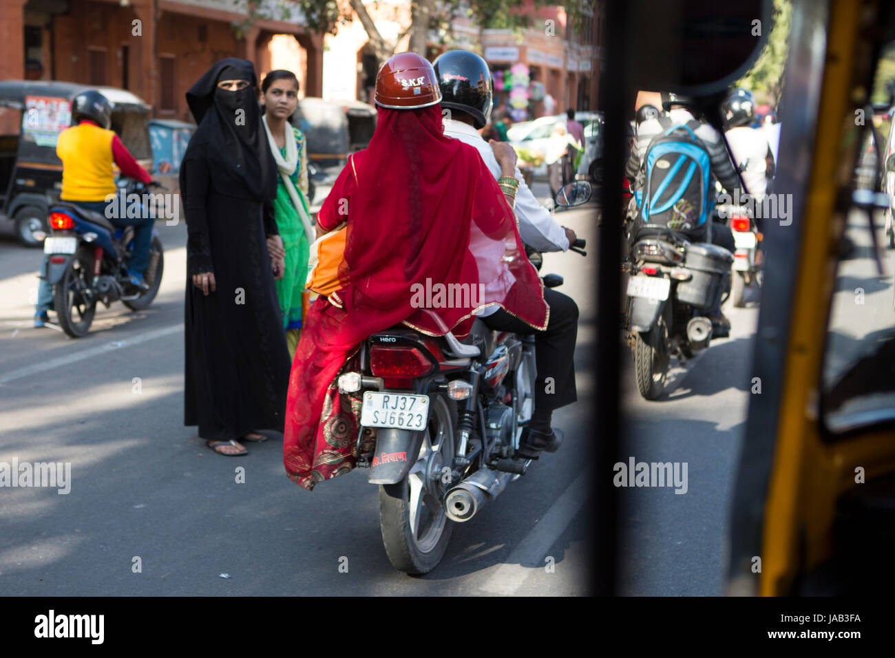 Une dame en Sari rouge côté équitation selle sur le dos d'une moto à Jaipur, Inde Banque D'Images