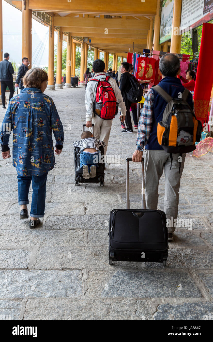 Yangshuo, Chine. Petit garçon attraper un tour sur la valise de son père. Banque D'Images