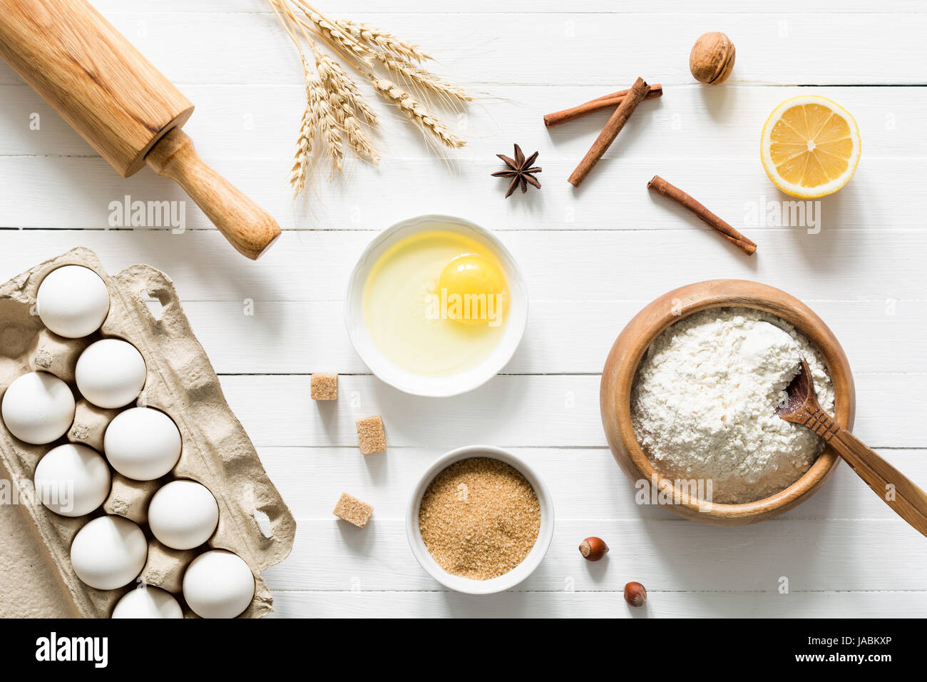 Ingrédients de cuisson sur table en bois blanc. Les œufs, la cassonade, la farine blanche, les épis de blé, épices, noix et citron sur blanc. Vue de dessus de table Banque D'Images