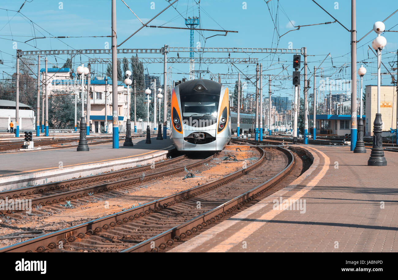 High speed train arrive sur la gare au coucher du soleil en Europe. Train intercity modernes sur le quai de la gare. Paysage industriel avec passeng Banque D'Images