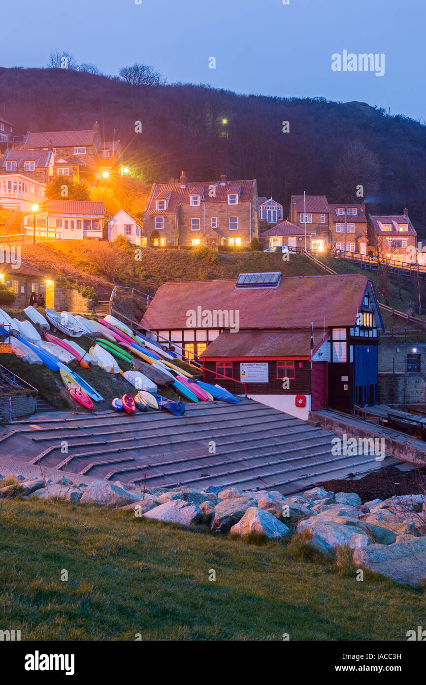 Joli village côtier pittoresque (soir) sont allumés dans maisons & bord de bateaux colorés sont sur cale - Runswick Bay, Yorkshire, Angleterre, Royaume-Uni. Banque D'Images